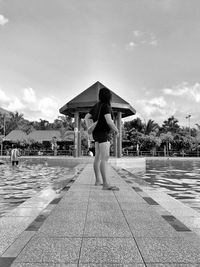Rear view of boy standing at swimming pool against sky