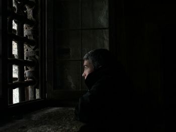 Side view of thoughtful man looking away while standing by window in prison