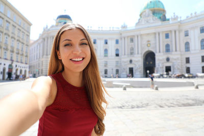 Portrait of smiling young woman standing against building in city