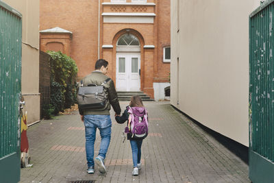 Rear view of father and daughter with backpack walking towards school