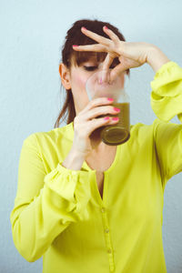 Midsection of young woman holding yellow while standing against wall