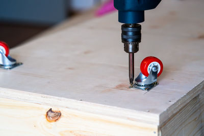 Close-up of electrical screwdriver fixing castor wheel on a wooden table.