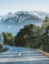 Road amidst trees and snowcapped mountains against sky