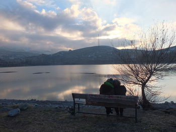 Rear view of couple sitting on lake against sky