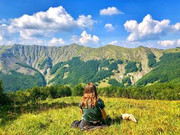 Rear view of woman sitting on mountain against sky