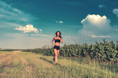 Woman running across field. short black shorts and top. sunny day. the sky in background person