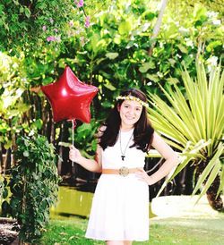 Portrait of young woman holding star shape balloon while standing at backyard