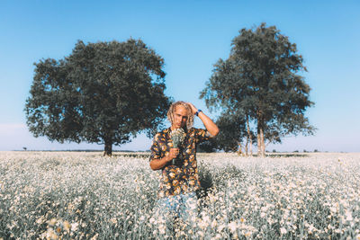 Man smelling flowers while standing against sky