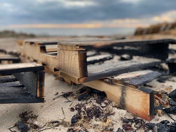 Close-up of burning wood pallet on the beach with water and beach grass in the background.