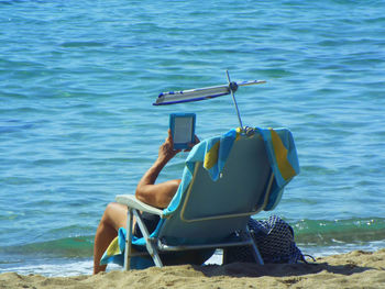 Man using digital tablet while lying on deck chair at beach