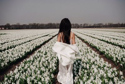 Woman standing by flowering plants against sky