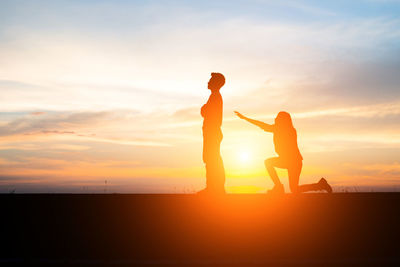 Silhouette man and woman against sky during sunset