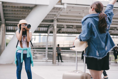 Tourists photographing friend standing on footpath in city