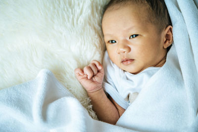 Close-up of baby lying on bed wrapped in blanket at home