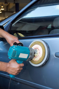 Cropped hands of man polishing car in auto repair shop