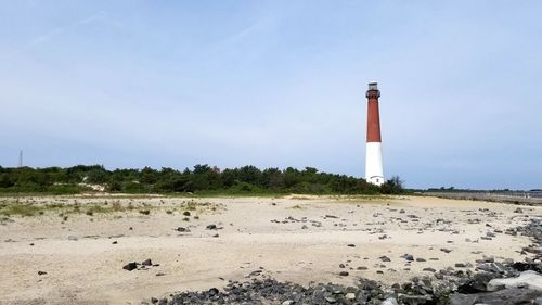 Lighthouse on beach by building against sky
