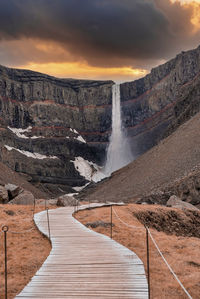 Walkway leading towards beautiful hengifoss waterfall against sky during sunset