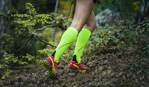 Legs female runner in bright green compression socks run uphill in forest