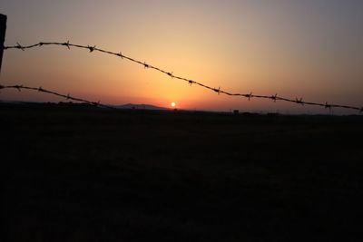 Silhouette of barbed wire against sky during sunset