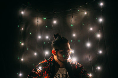 Man amidst illuminated fairy lights against wall