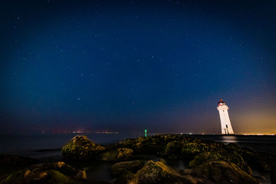 Lighthouse by sea against sky at night