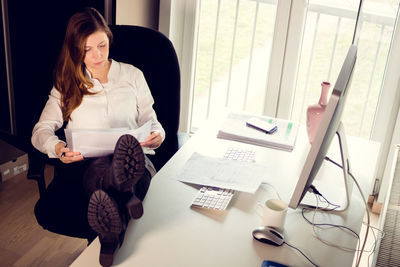 Full length of businesswoman reading paper on table in office