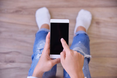 Low section of woman using mobile phone on hardwood floor