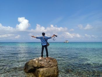 Man standing on rock by sea against sky