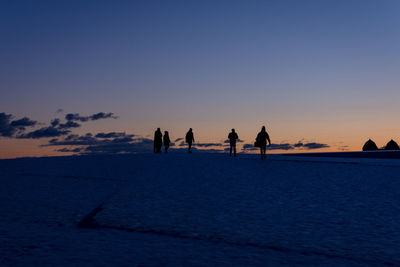 Silhouette people on land against sky during sunset