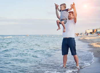 Father picking up son while standing at beach