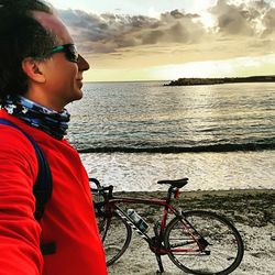 Side view of man bicycling on beach against sky during sunset