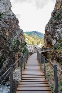 Walkway leading towards mountains against sky