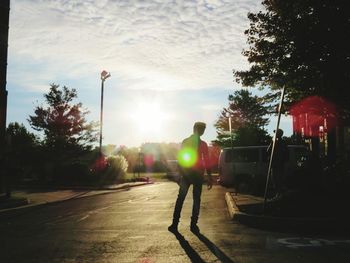 Man standing on road amidst trees against sky