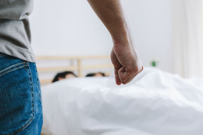 Cropped image of man clenching fist against couple sleeping on bed