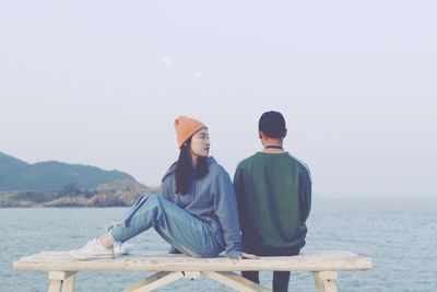 Rear view of woman sitting on sea against clear sky