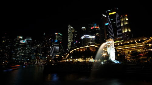 Fountain against illuminated modern buildings in city at night