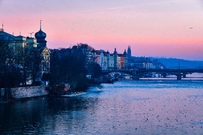 Buildings by river against sky during sunset