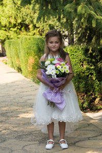 Full length portrait of girl holding bouquet while standing outdoors