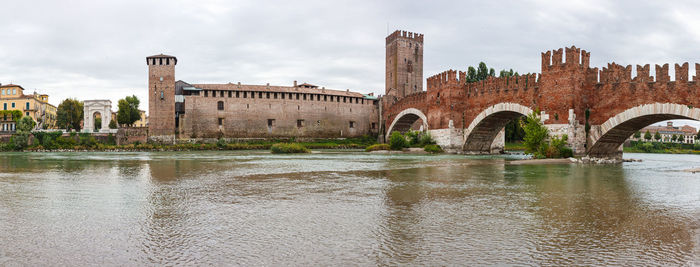 Arch bridge over river by buildings against sky