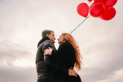 Rear view of couple with balloons against sky