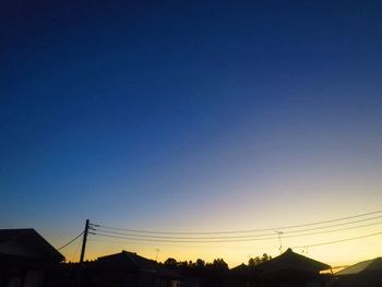 Low angle view of silhouette electricity pylon against clear sky