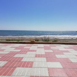 Footpath by sea against clear blue sky