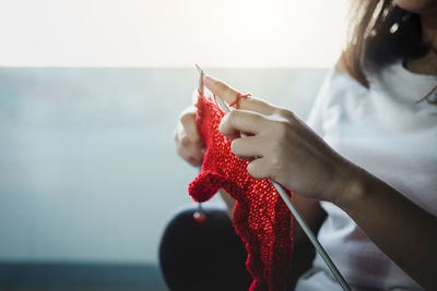 Midsection of woman knitting red wool at home