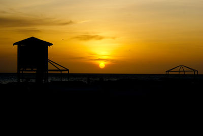 Silhouette beach by sea against sky during sunset