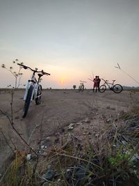 People riding bicycle on field against sky during sunset