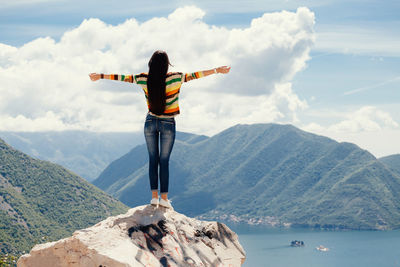 Rear view of woman with arms outstretched standing on cliff by sea