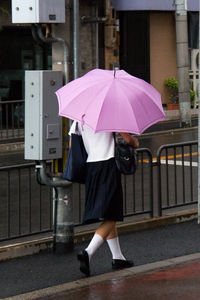 Rear view of schoolgirl under umbrella walking in footpath in rainy season
