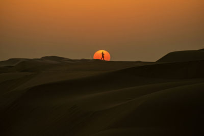 Mid distance of man on landscape against sky during sunset