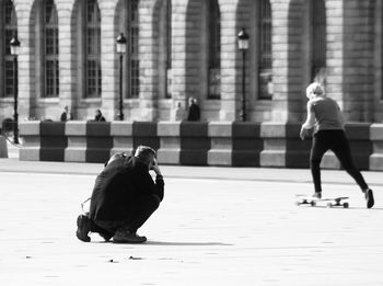Man photographing while woman skateboarding in city