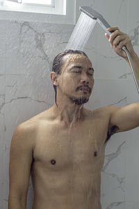 Shirtless man taking shower in bathroom